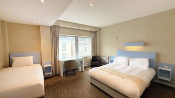 A hotel room with two beds, a desk, a chair, and a window.