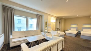 A hotel room with a sofa, armchairs, a small table, a bed, a mirror, and a view of the outside. - Citrus Hotel Cheltenham by Compass Hospitality (Cheltenham)