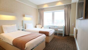 A hotel room with two beds, a desk, a chair, a large window with curtains, and a flat-screen TV mounted on the wall.