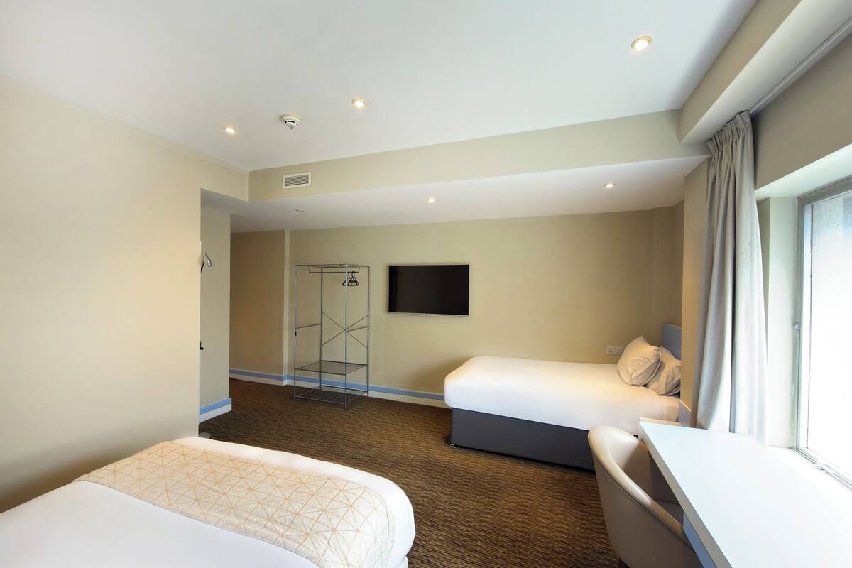 A hotel room with two beds, a desk, a shower area, and a TV.