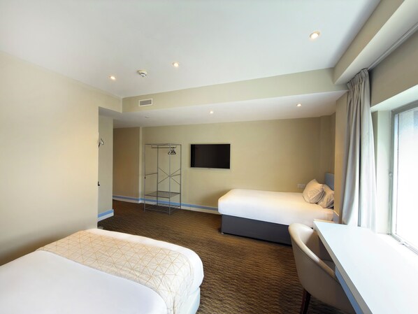 Habitación de hotel con dos camas, un escritorio, zona de ducha y televisor.