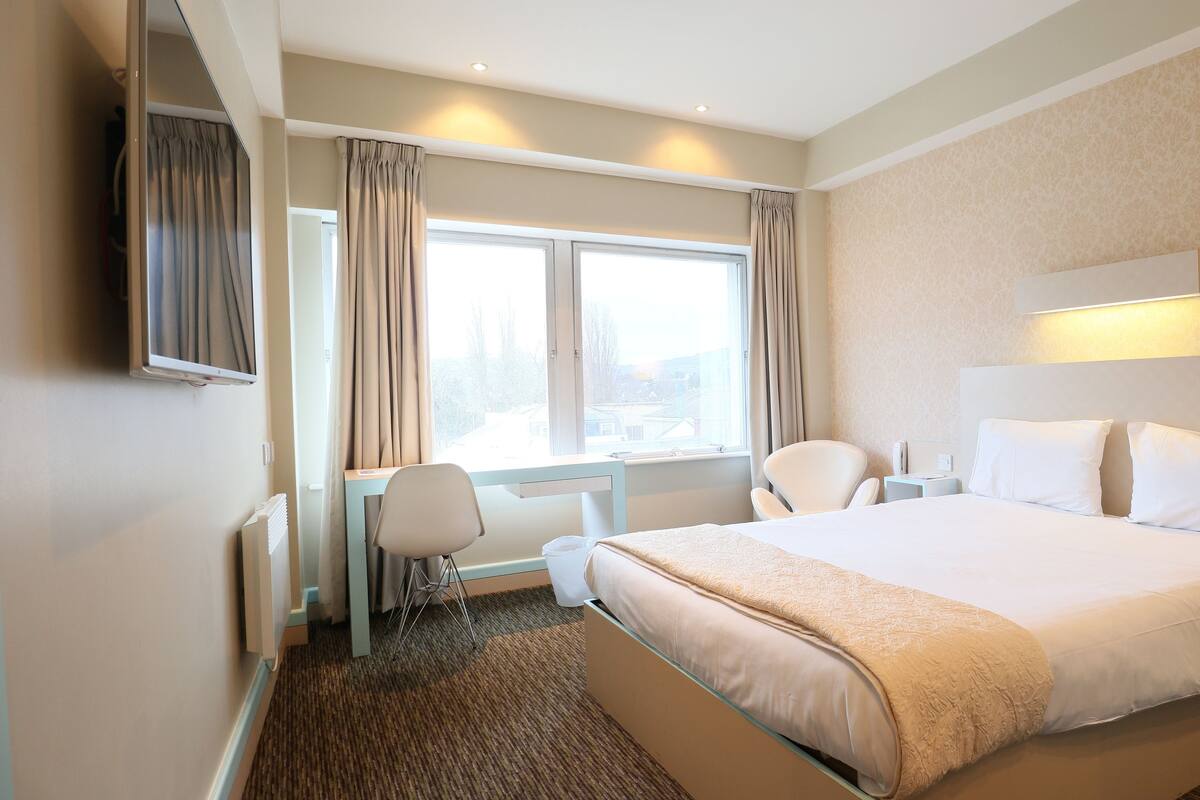 A hotel room with a bed, a desk, a chair, and a window with curtains.