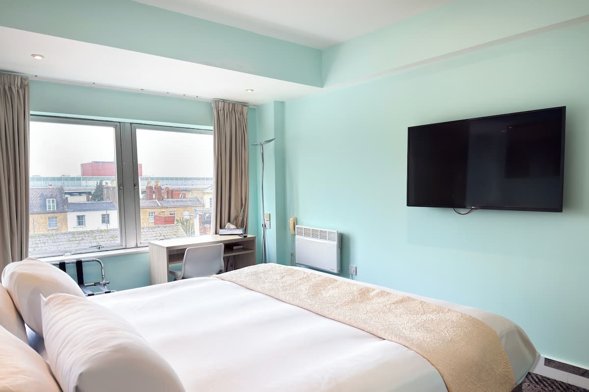 A hotel room with a bed, a desk, a chair, a TV, and a window with curtains.