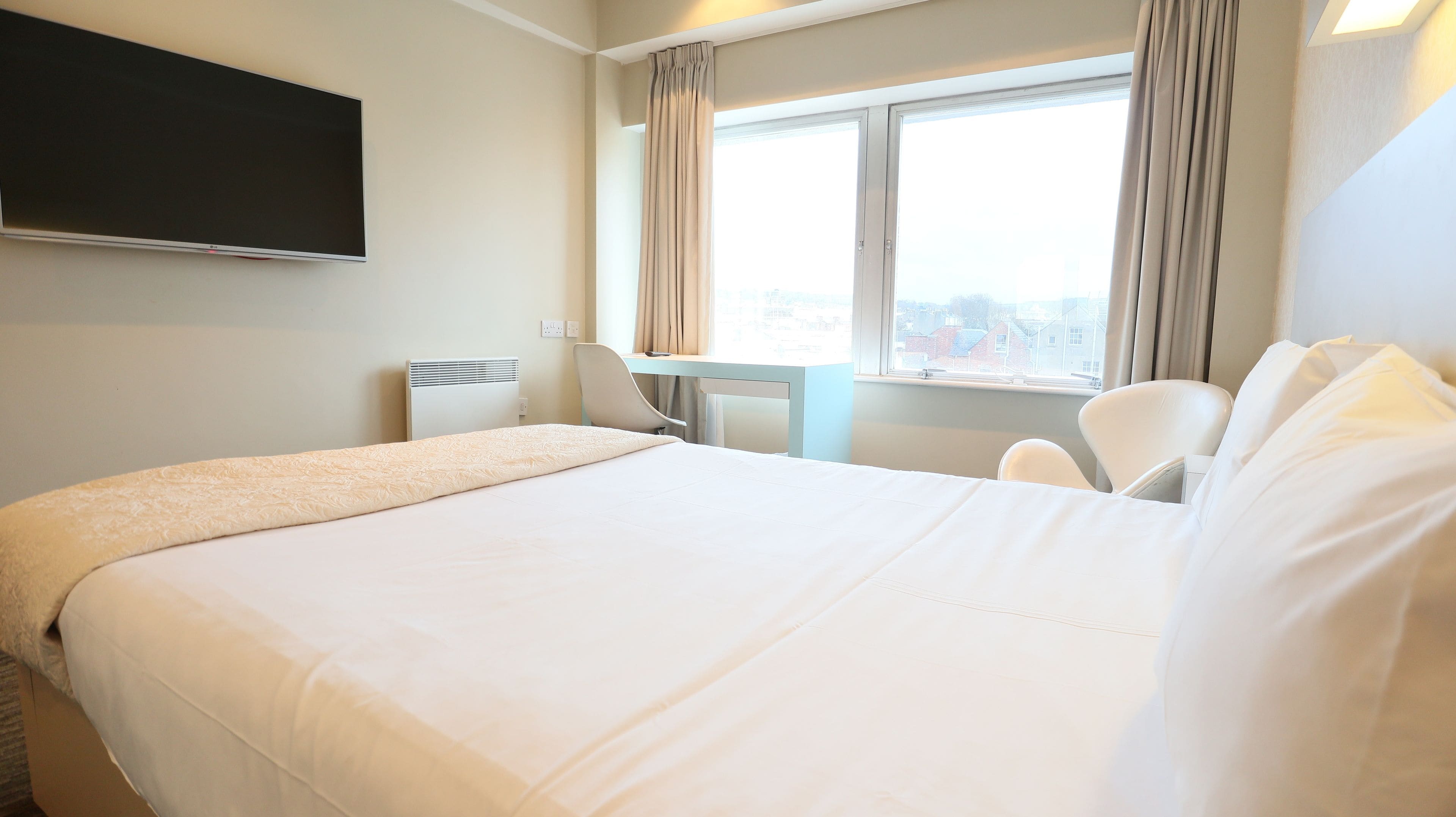 A hotel room with a large bed, a desk, a chair, a flat-screen TV, and a window with curtains.