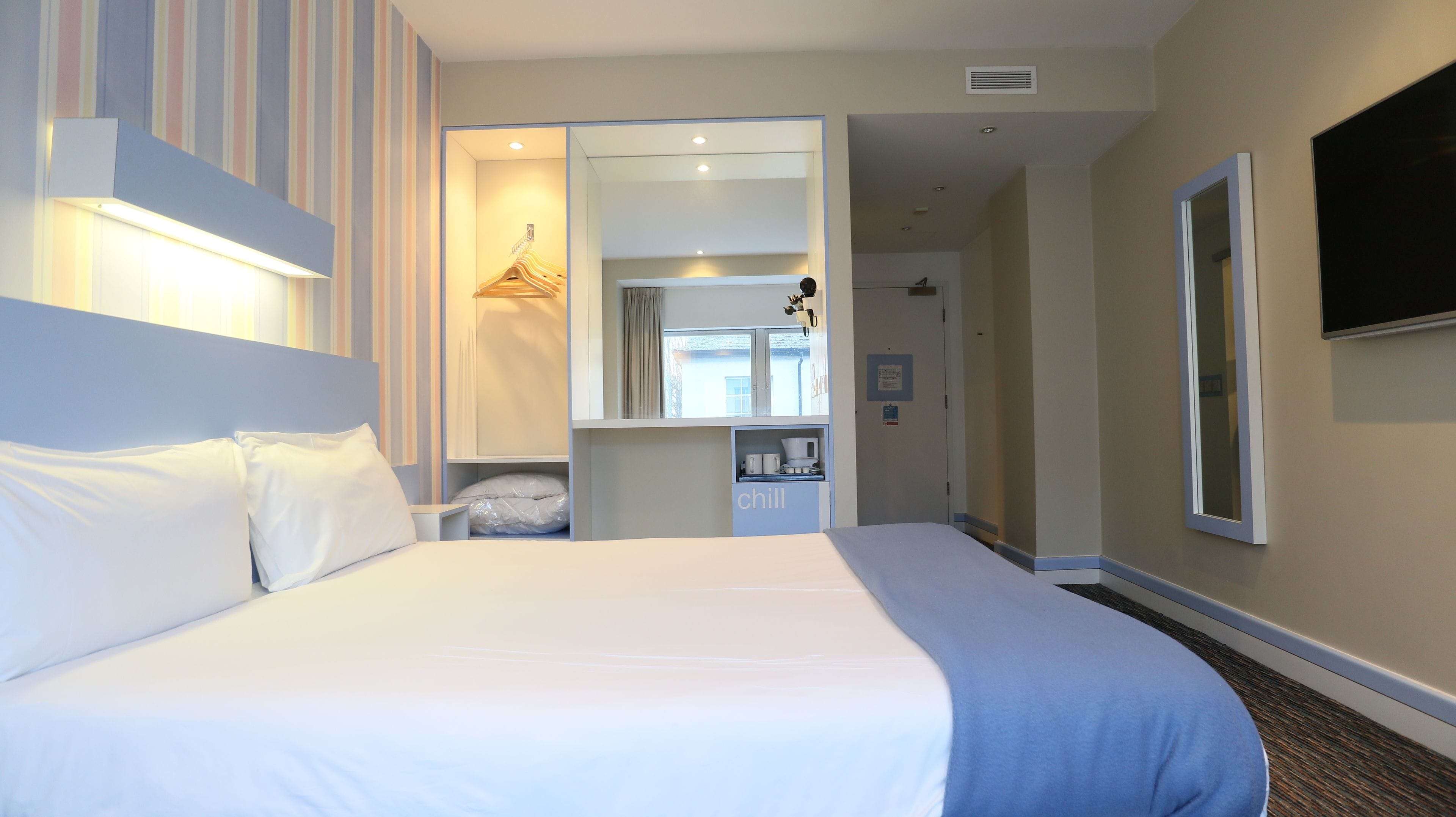 A hotel room with a large bed, a wardrobe, a mirror, and a television on the wall.