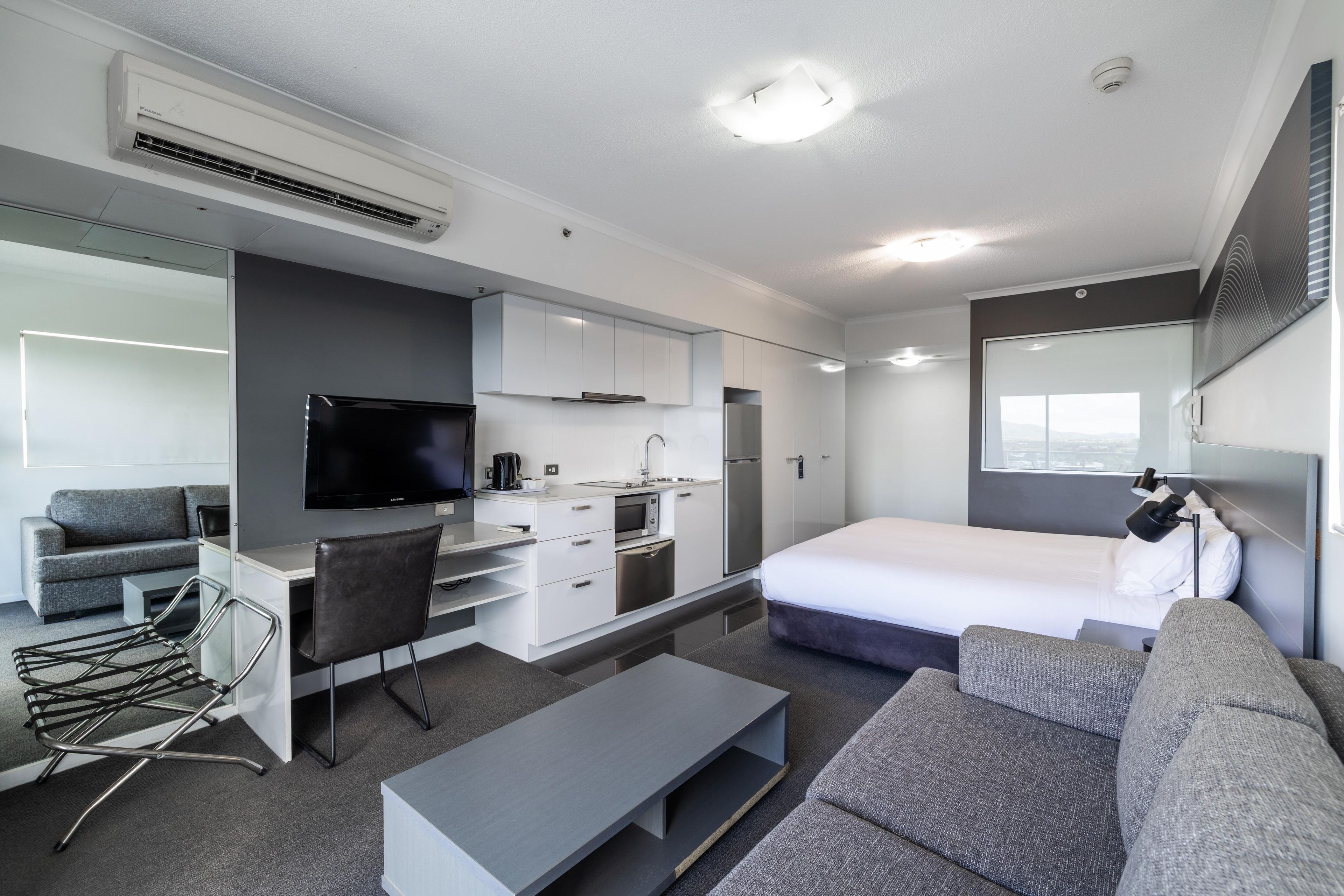 Ein modernes Hotelzimmer mit Flachbildfernseher, einer Küchenzeile, einem Bett und einer Sitzecke.