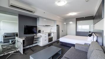 Ein modernes Hotelzimmer mit Flachbildfernseher, einer Küchenzeile, einem Bett und einer Sitzecke.