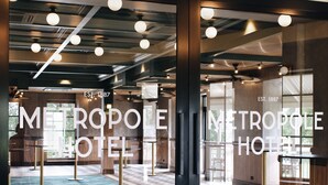 Interior moderno de un hotel con puertas de vidrio, piso a cuadros y un letrero visible que dice "METROPOLI HOTEL".