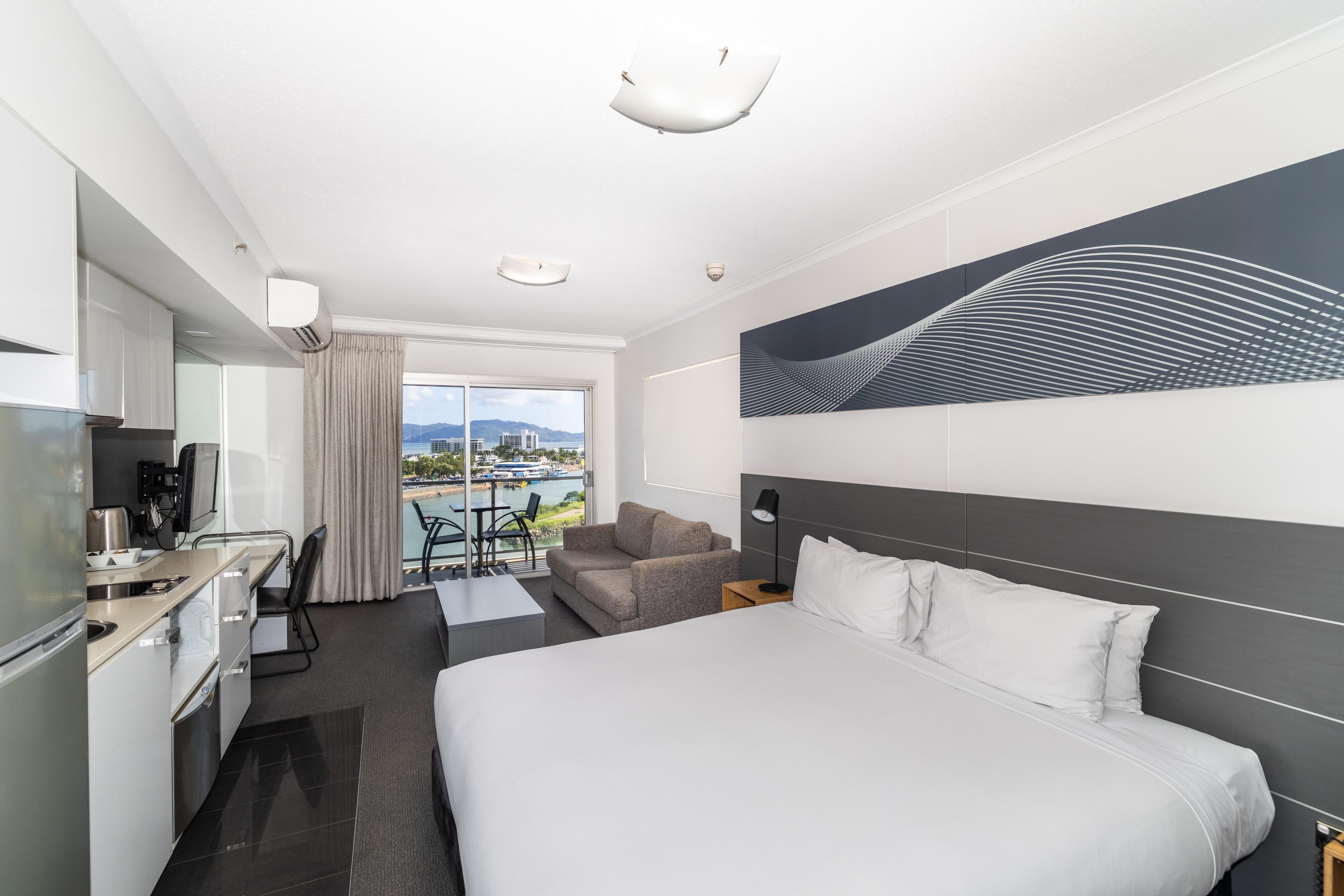 A hotel room with a bed, a desk, a chair, a sofa, a view of the city, and a large abstract painting on the wall.