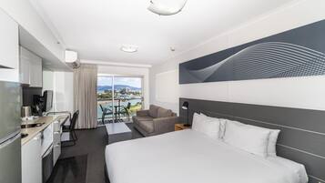 A hotel room with a bed, a desk, a chair, a sofa, a view of the city, and a large abstract painting on the wall.