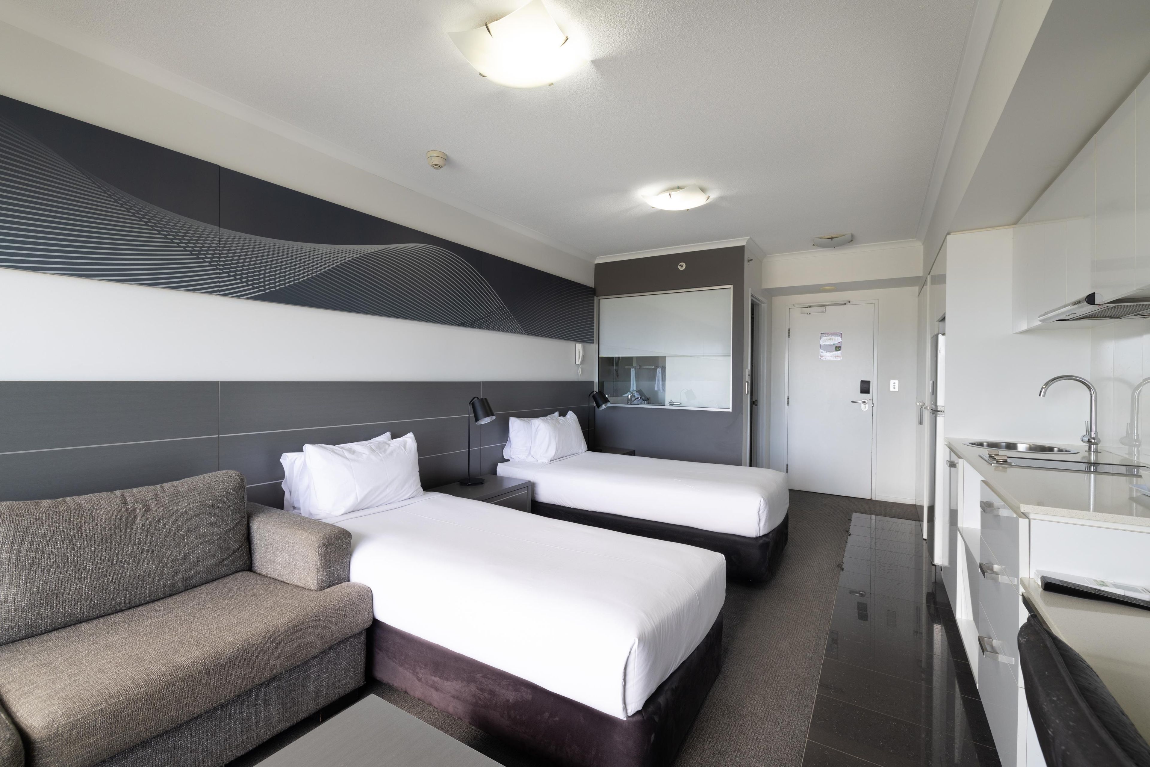 A hotel room with two beds, a sofa, a bathroom, and a kitchenette.