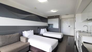 A hotel room with two beds, a sofa, a bathroom, and a kitchenette.
