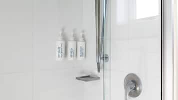 A bathroom with a glass shower enclosure, a handheld showerhead, and three bottles of shampoo and conditioner.