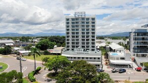 A modern hotel with a rooftop pool, surrounded by lush greenery and a view of distant mountains.