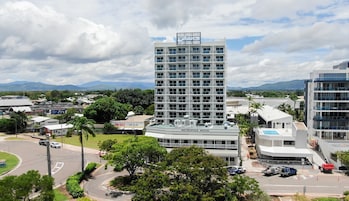 Un hotel moderno con piscina en la azotea, rodeado de exuberante vegetación y vistas a montañas distantes.