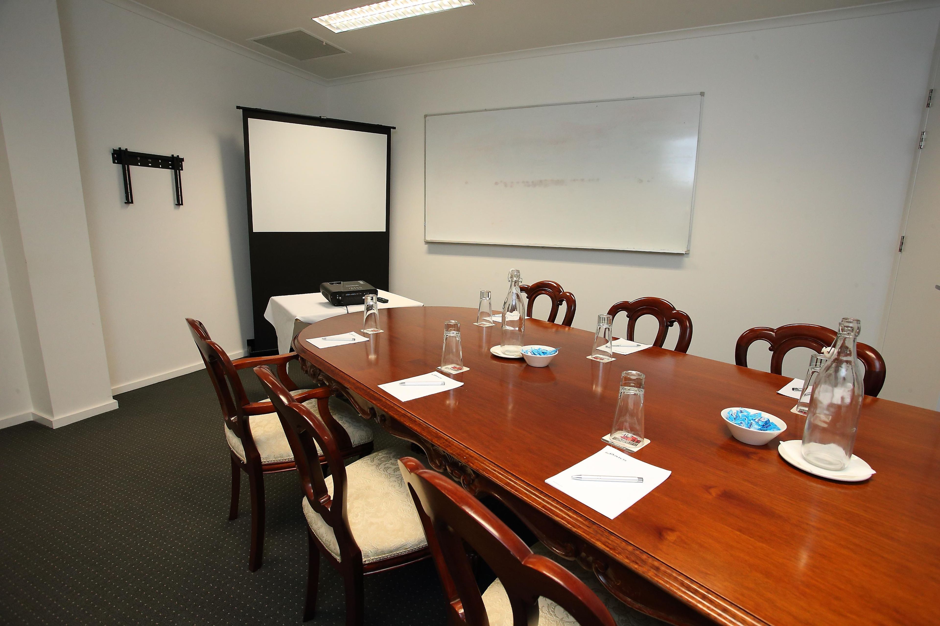 A conference room with a long wooden table, chairs, a projector, and a whiteboard.