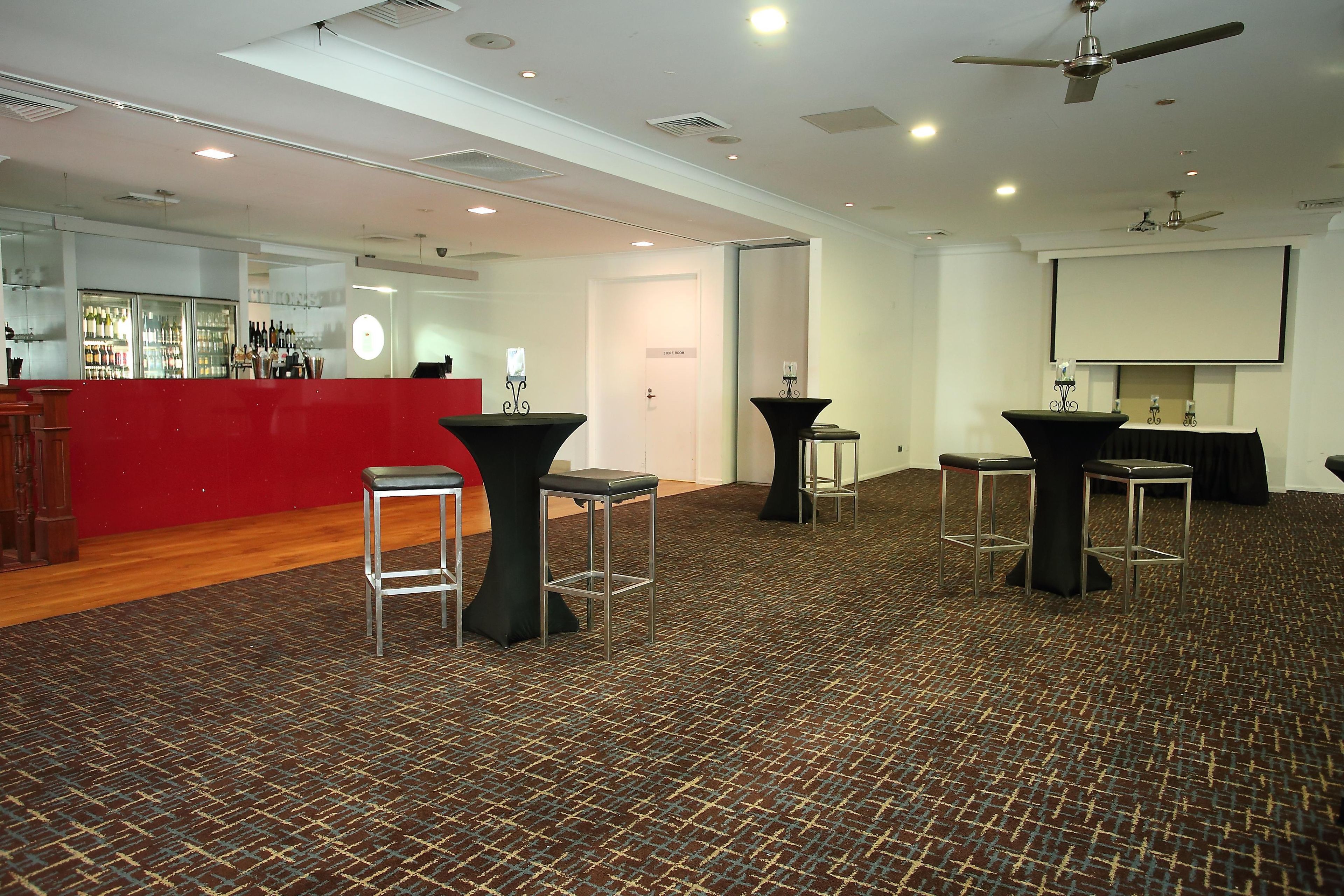 A spacious room with a bar area, multiple tables, and chairs, and a projector screen on the wall.