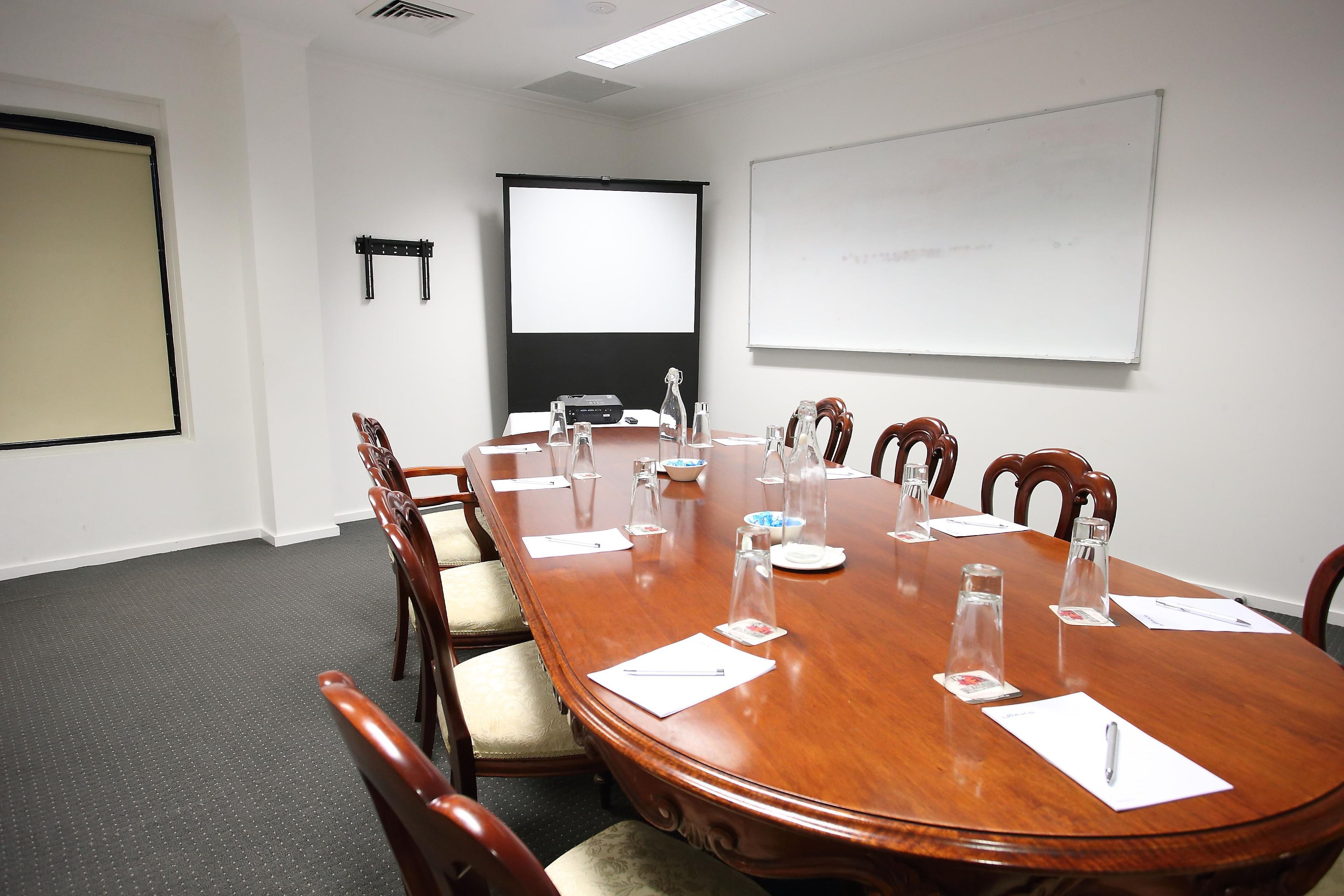 A conference room with a long wooden table, chairs, a projector screen, and a whiteboard.