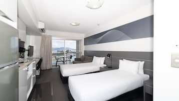A hotel room with two beds, a desk, a chair, and a view of the city.