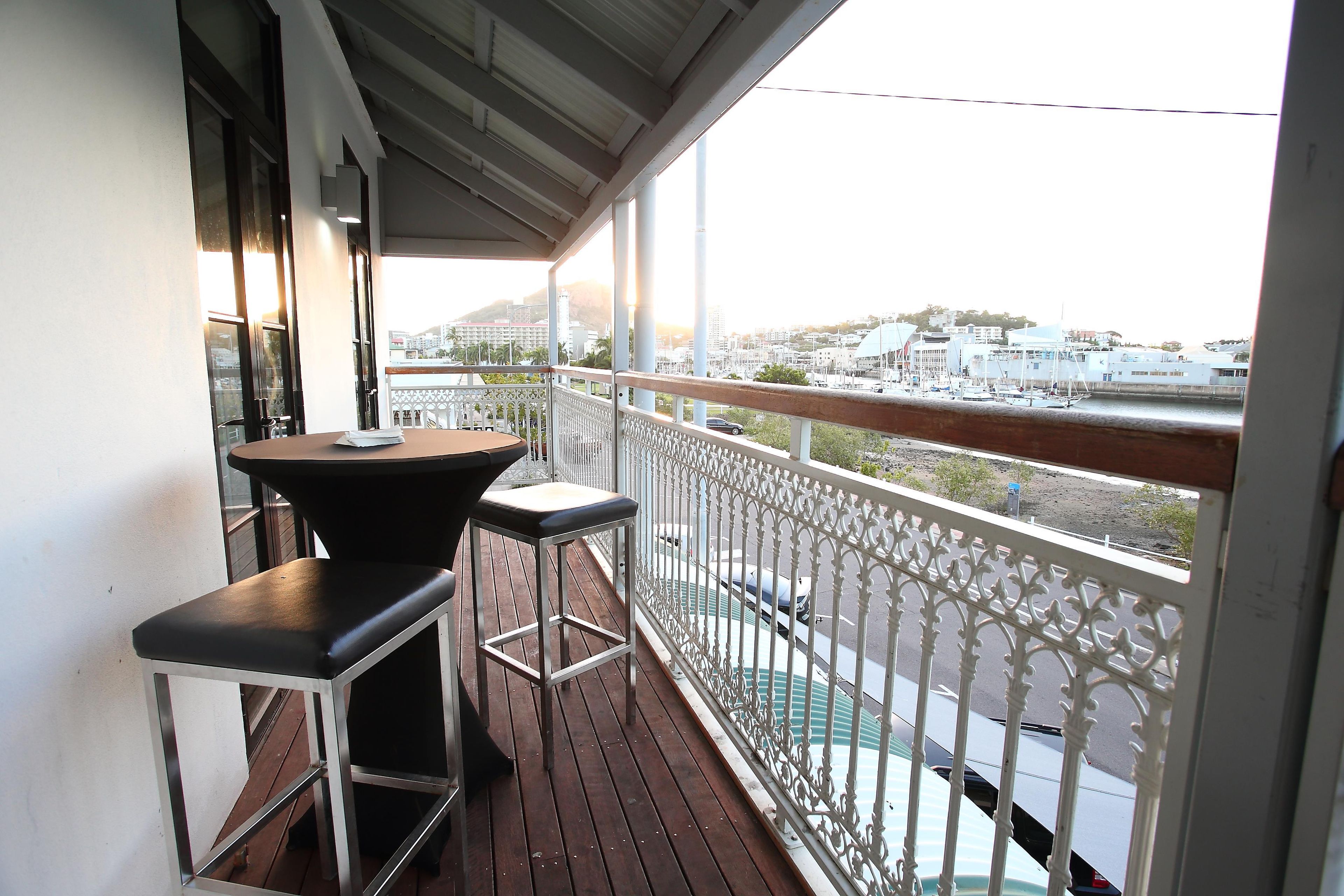 A balcony with a table and two chairs, overlooking a marina with boats.