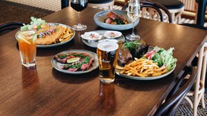 Un ambiente de restaurante con una zona de bar al fondo, que incluye estantes con botellas y una parrilla.