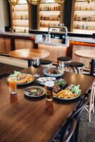 Un ambiente de restaurante con una zona de bar al fondo, que incluye estantes con botellas y una parrilla.