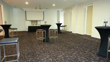 A conference room with a carpeted floor, tables with stools, a projector screen, and ceiling fans.