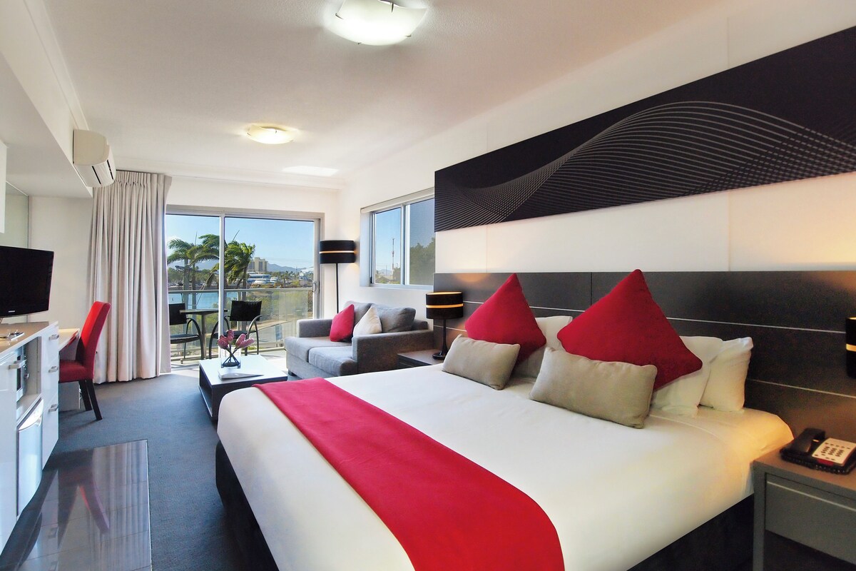 Habitación de hotel moderna con una cama grande, un escritorio, un televisor y un balcón con vistas.