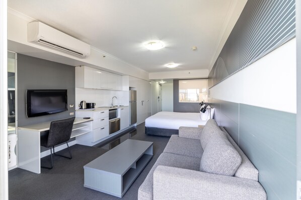 Una habitación de hotel moderna con televisión de pantalla plana, un sofá, una mesa de centro, kitchenette y una cama.