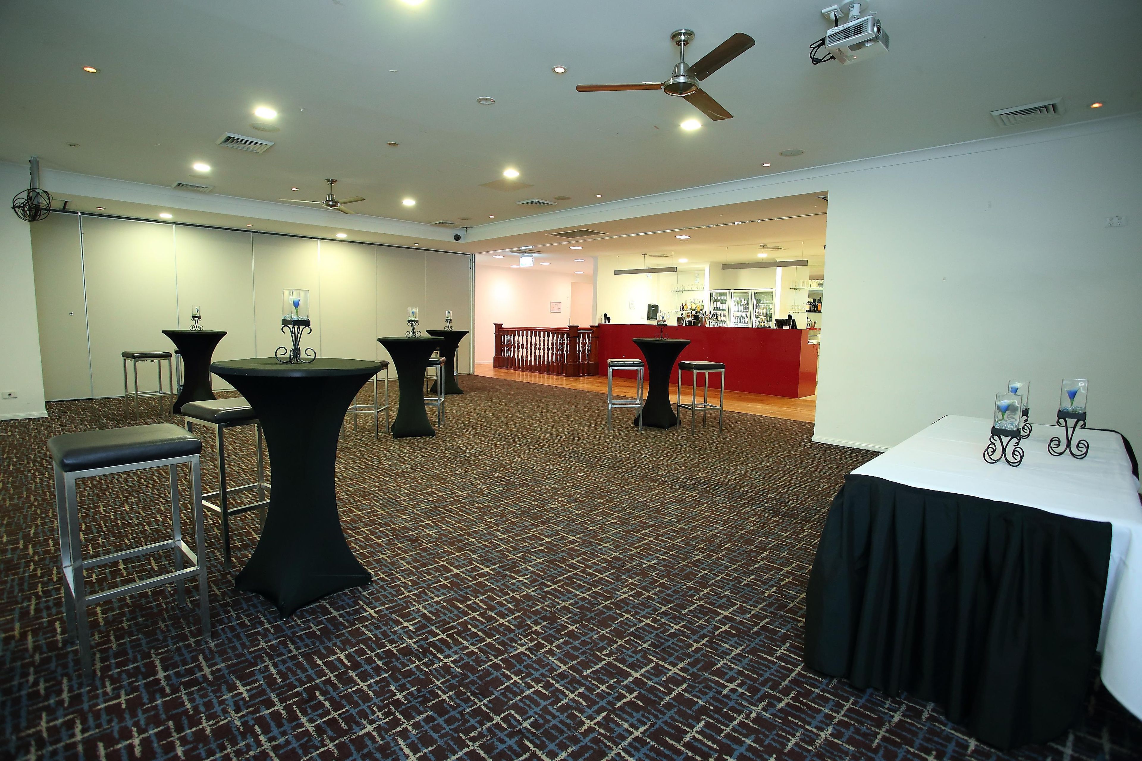 Sala de conferências com mesas, cadeiras, espaço de bar e ventilador de teto.