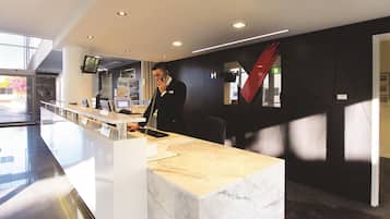 A modern hotel reception desk with a marble counter, a flat-screen TV, and a red abstract artwork on the wall.