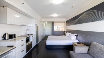Una habitación de hotel moderna con kitchenette, una cama, un sofá y un ventanal grande.