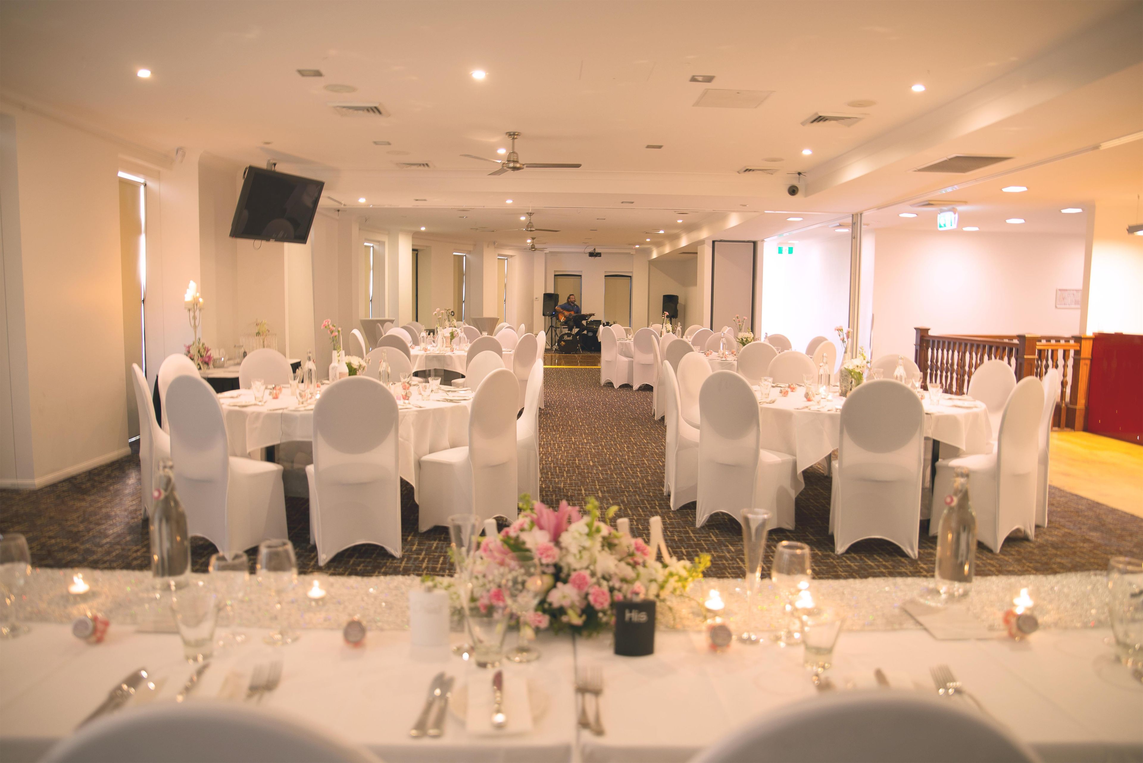 A banquet hall with multiple round tables set for dining, white chairs, and a stage area with a speaker system.