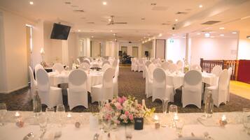 A banquet hall with multiple round tables set for dining, white chairs, and a stage area with a speaker system.