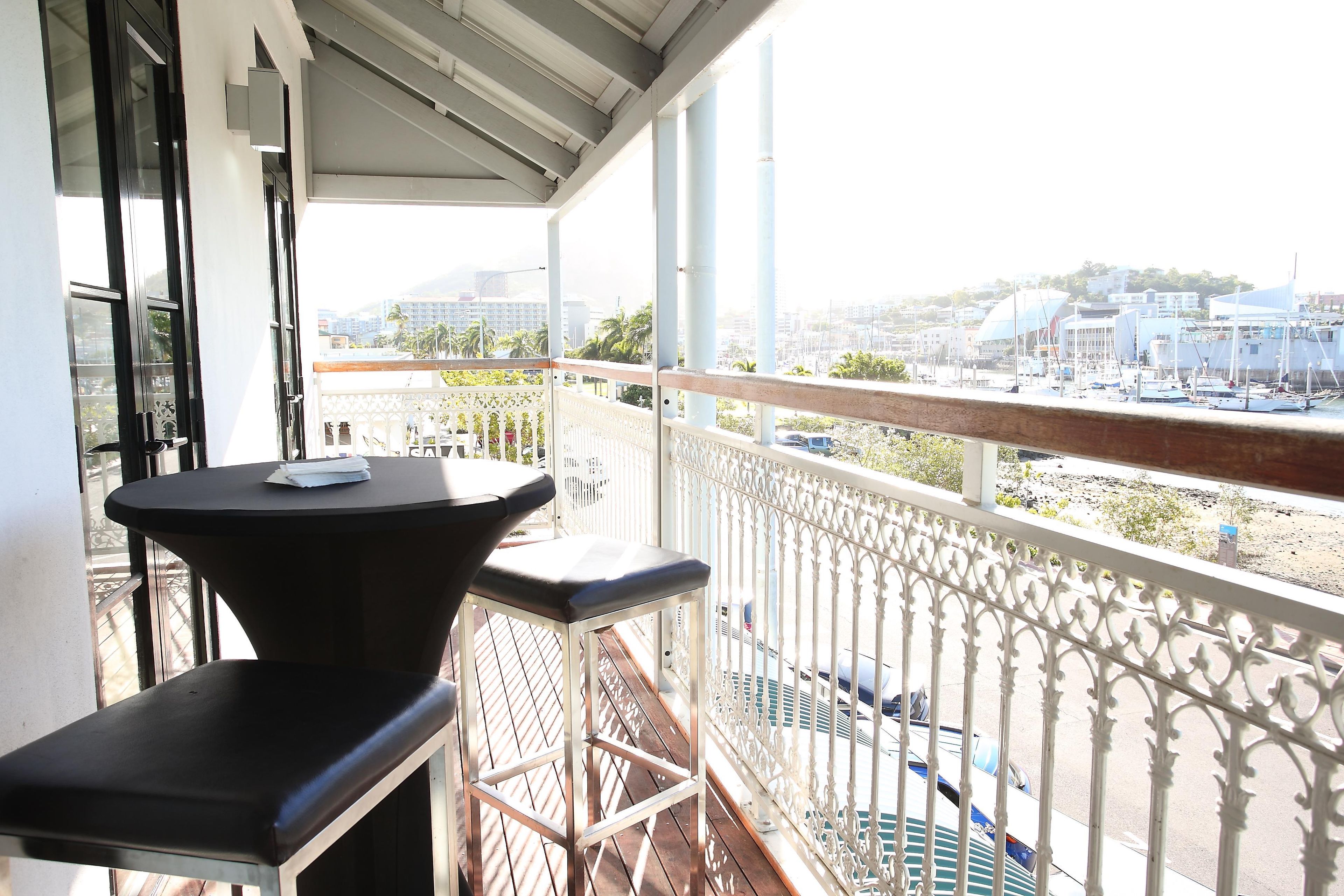 A balcony with a table and two chairs, overlooking a marina with boats and buildings.