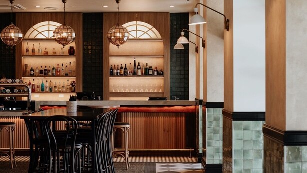 Una zona de bar con mostrador, taburetes y una variedad de botellas.