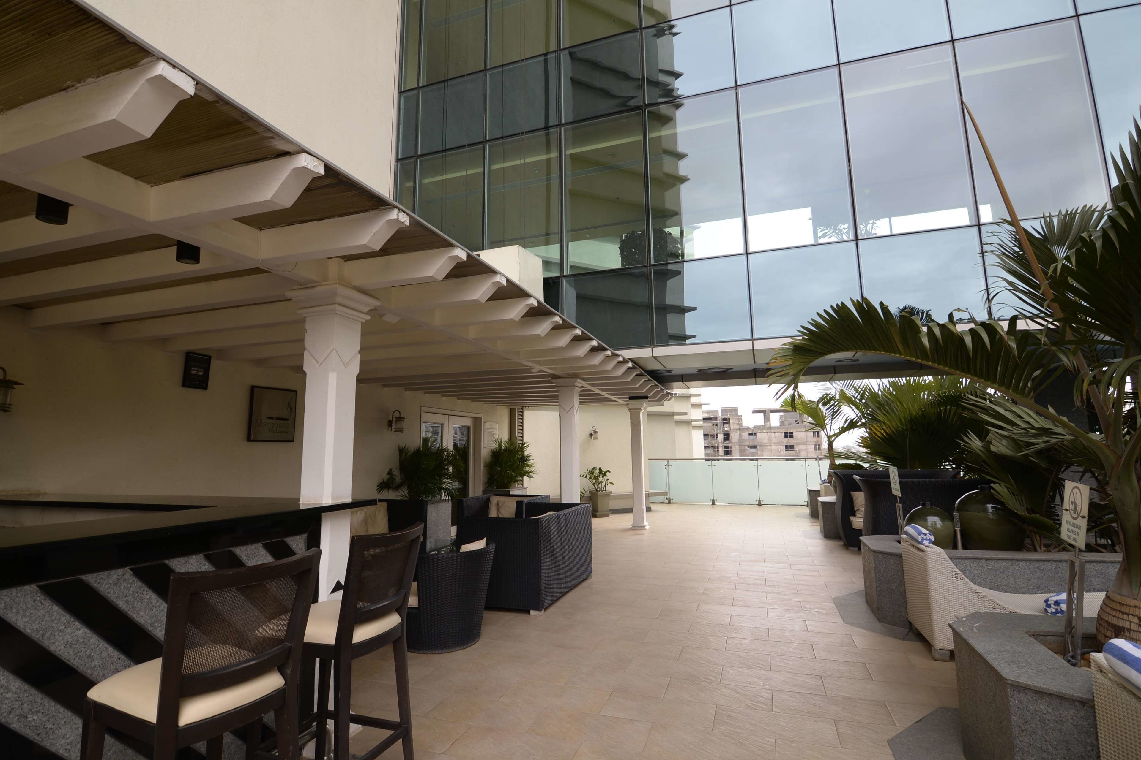 A spacious indoor area with a modern design, featuring a large glass wall, seating arrangements, and potted plants.