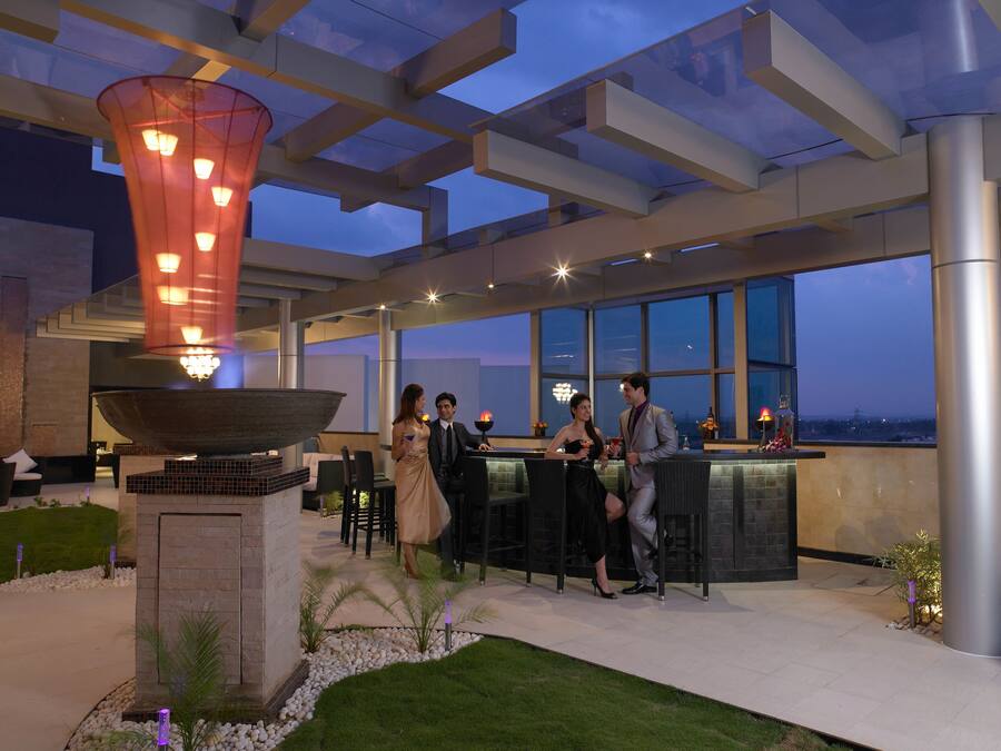 Uma área de bar ao ar livre com uma grande peça central em tigela, assentos e vista para o horizonte da cidade ao anoitecer.