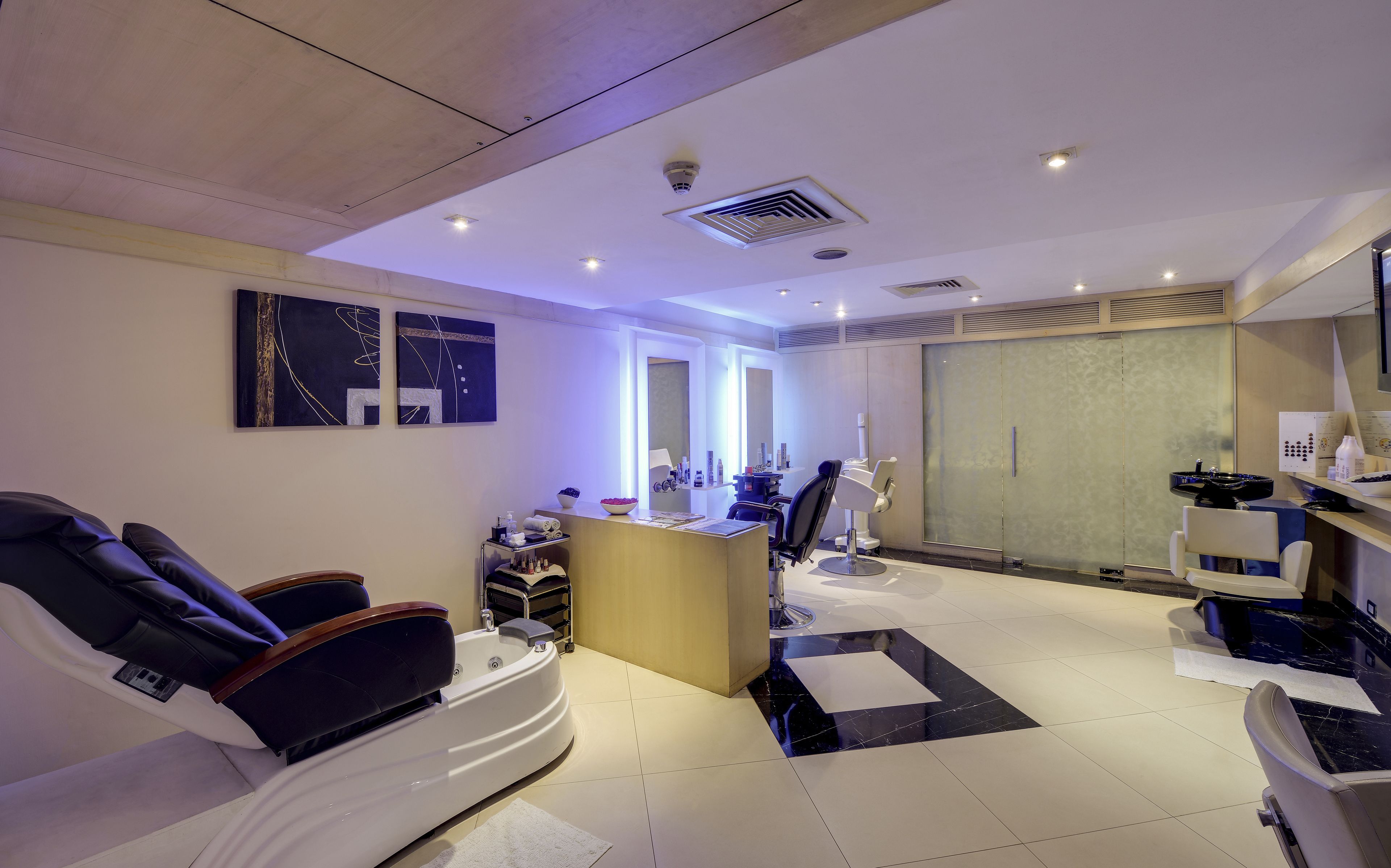 A modern spa room with a massage chair, a reception desk, and a large mirror.