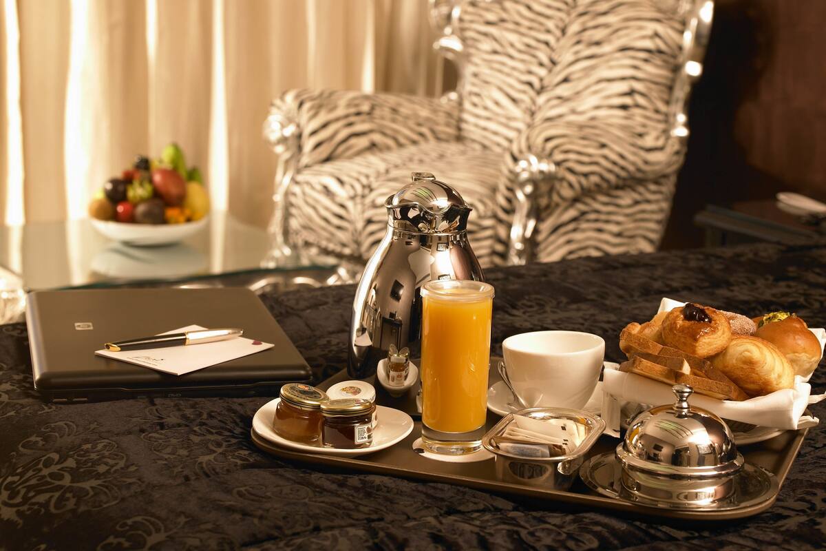 A breakfast tray with a laptop, a coffee pot, a glass of orange juice, a cup, and pastries on a table.