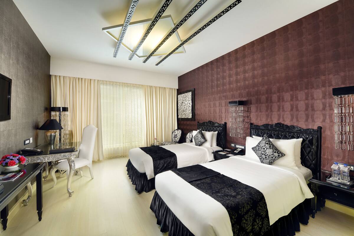 A hotel room with two beds, a desk, a chair, and a large window with curtains.