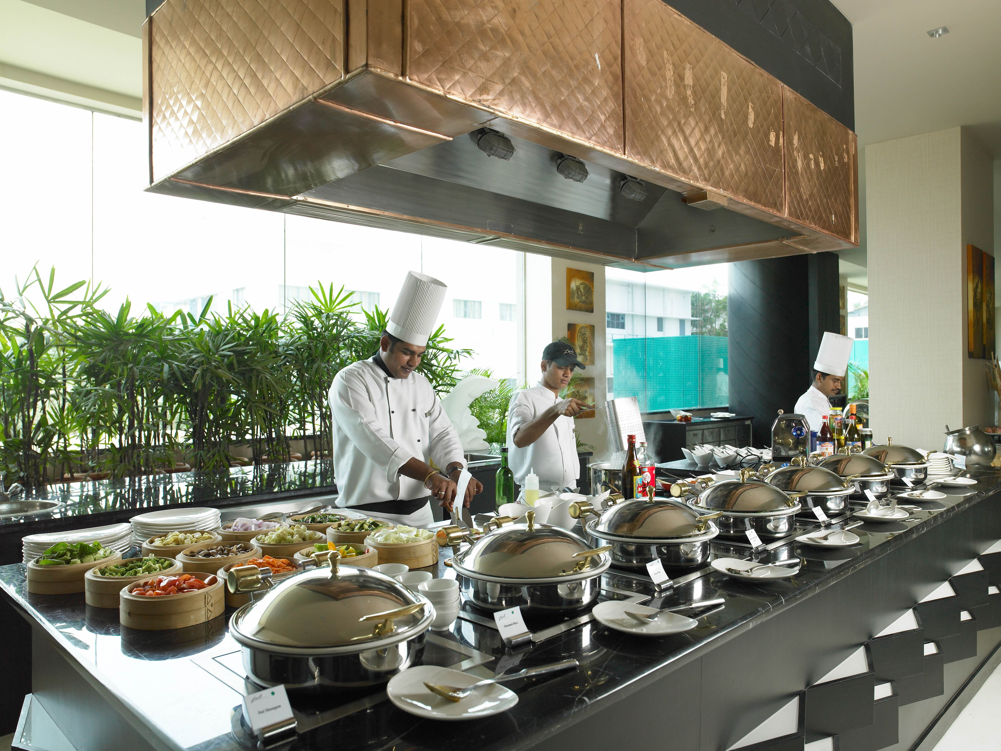 A buffet setup with multiple food stations, chefs in white uniforms, and a modern kitchen with copper fixtures.