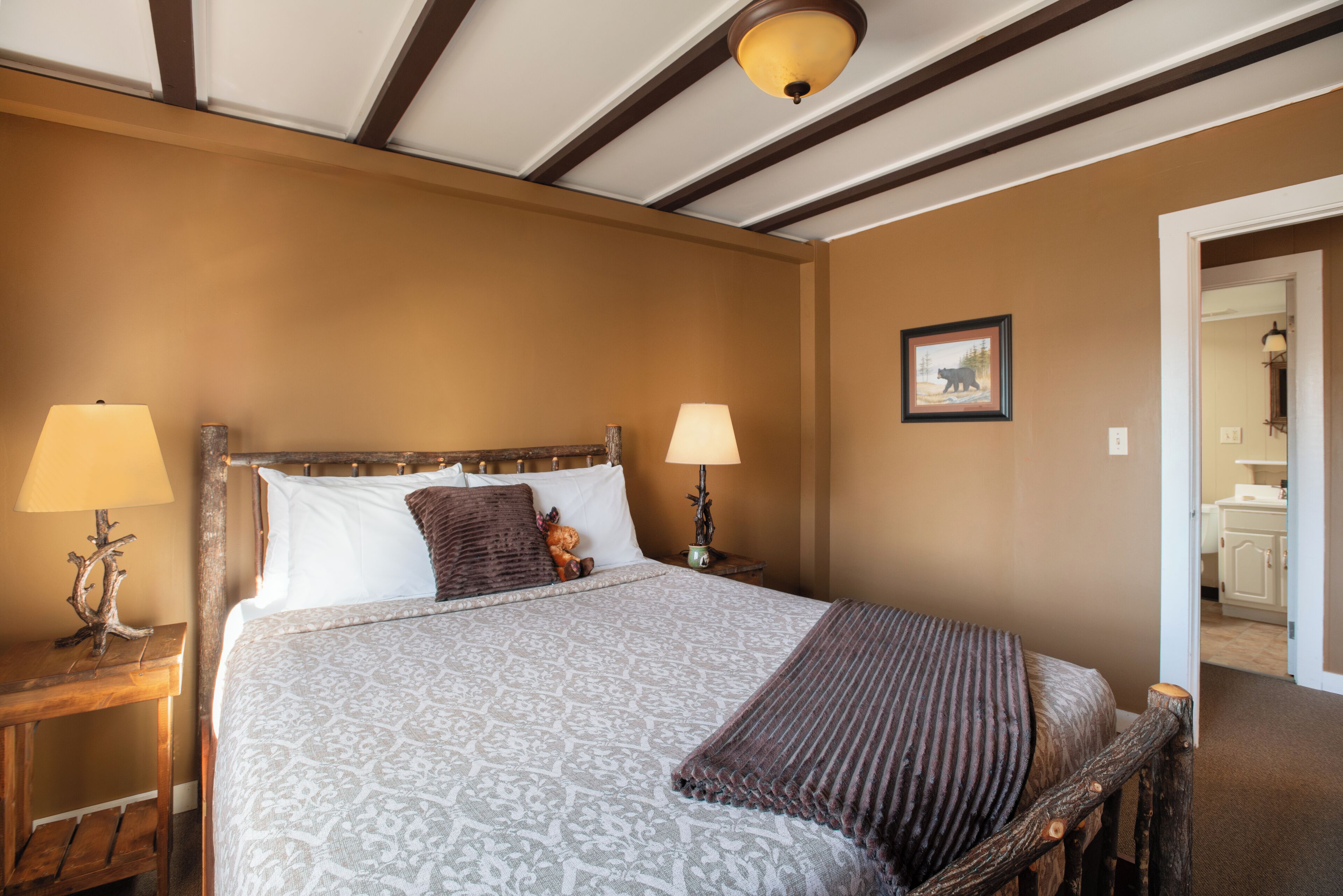 A bedroom with a wooden headboard, a patterned bedspread, two bedside lamps, and a framed picture on the wall.