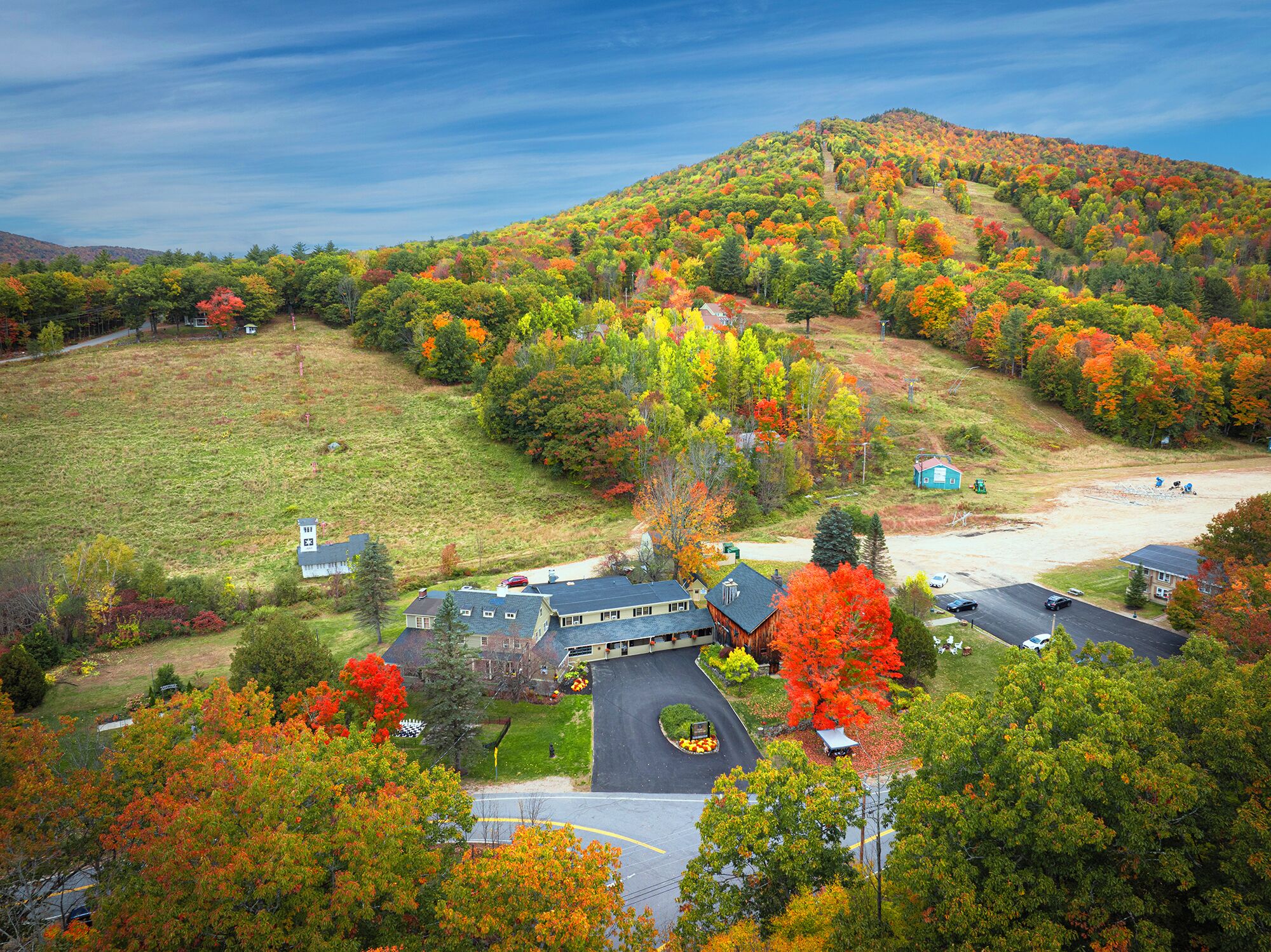 A large building with a parking lot, surrounded by autumn-colored trees and a hilly landscape.