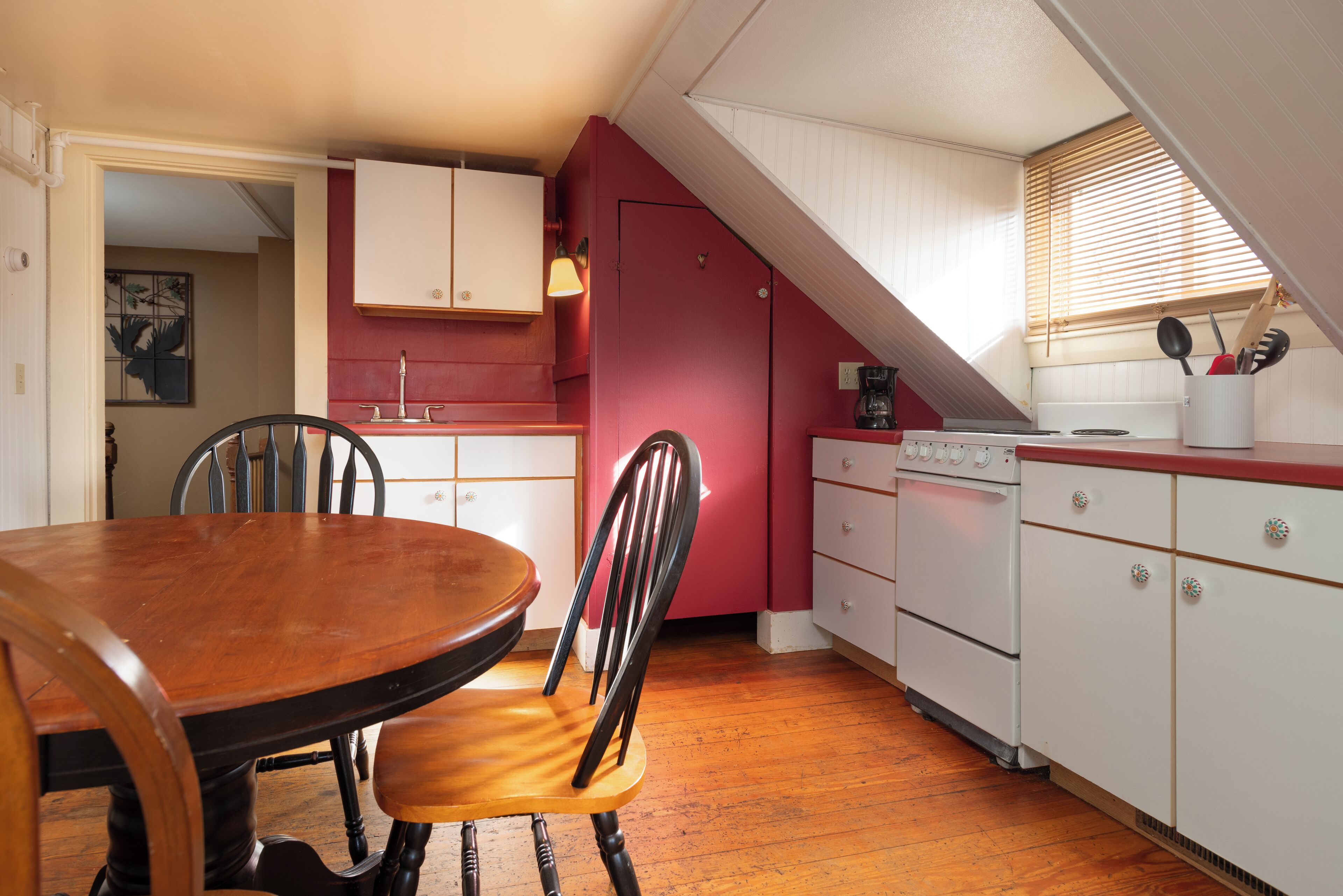 Une cuisine avec une table et des chaises en bois, des armoires blanches et un mur d’accent rouge.