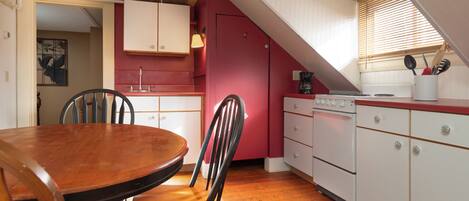 Une cuisine avec une table et des chaises en bois, des armoires blanches et un mur d’accent rouge.