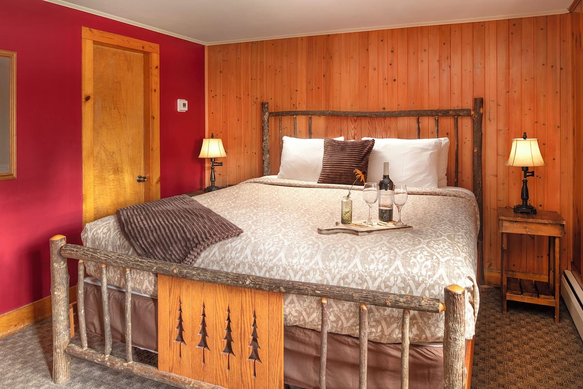 A wooden bed with a metal frame, two bedside lamps, a bedside table, and a red wall.