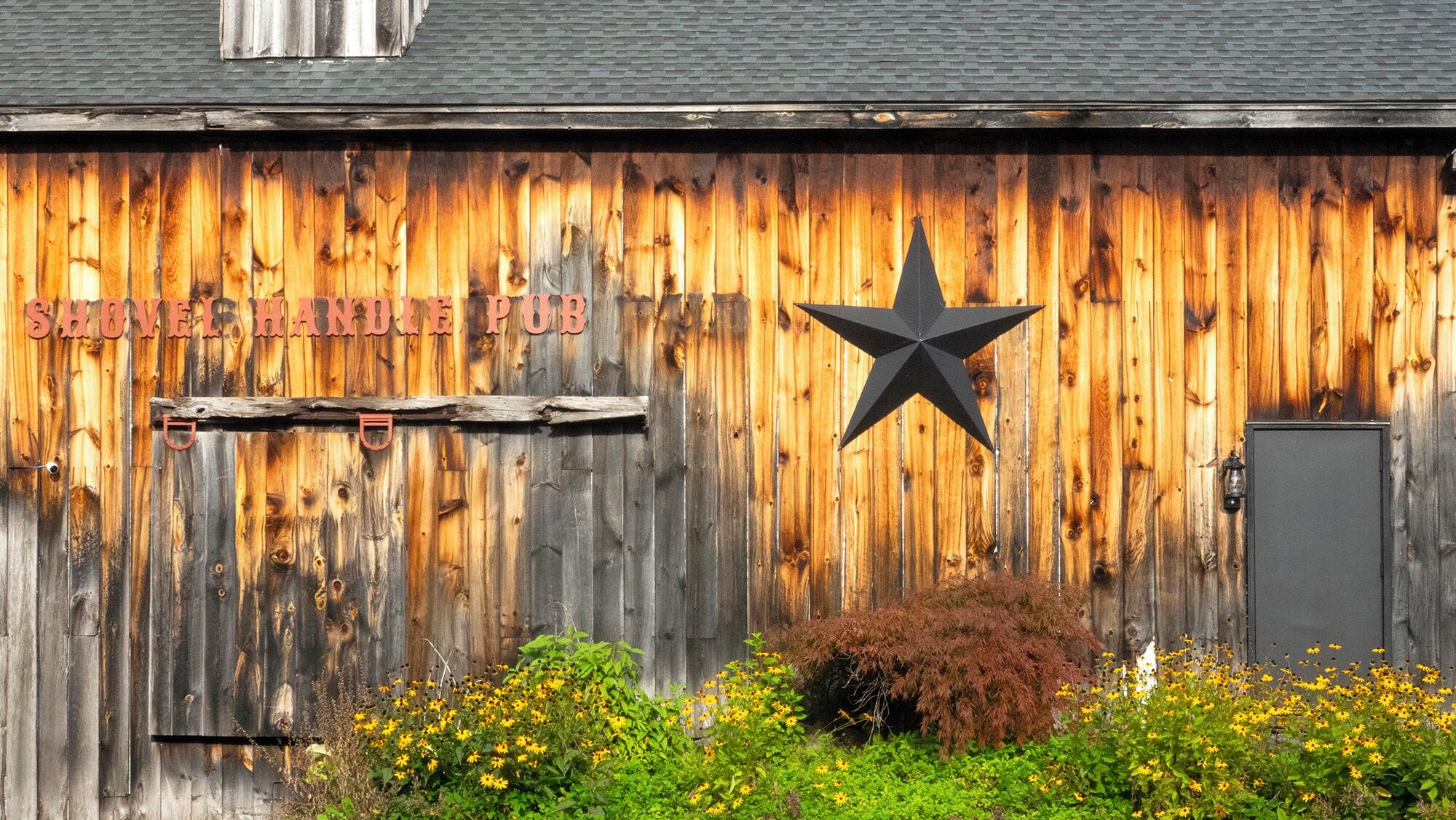 A rustic wooden building with a sign reading "SHOVEL HANDLE PUB" and a black star decoration.