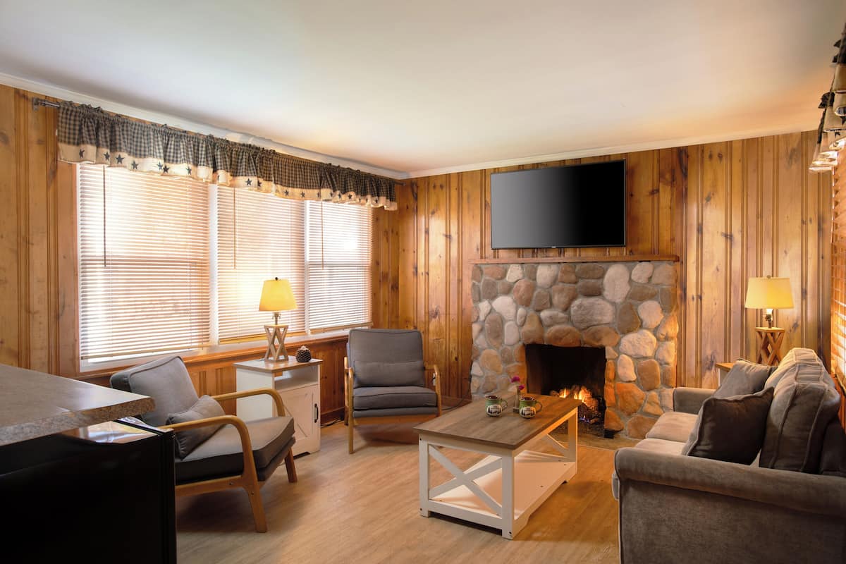A cozy living room with a stone fireplace, wooden walls, a flat-screen TV, and comfortable seating.