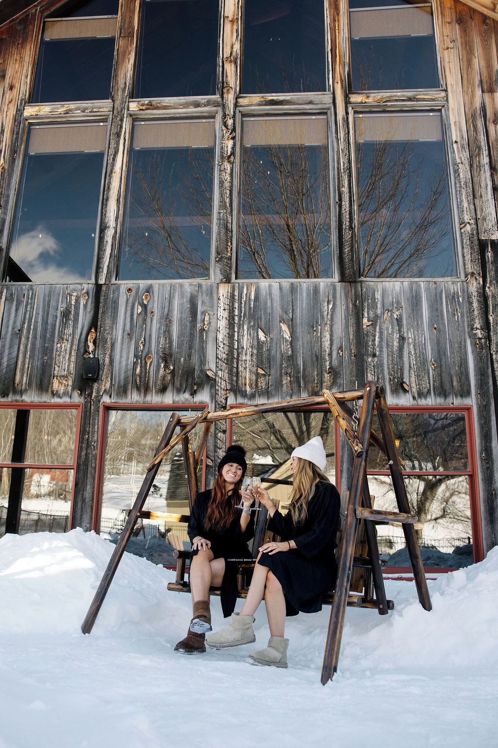 A rustic wooden building with large windows and a swing set in front.